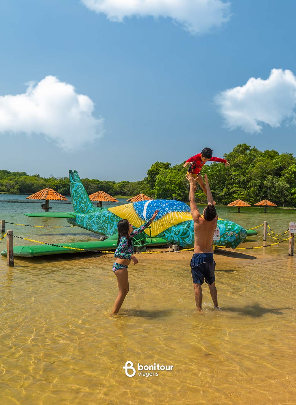 Casal brincando com criança em frente a avião estampado com bandeira do Brasil na praia da Figueira