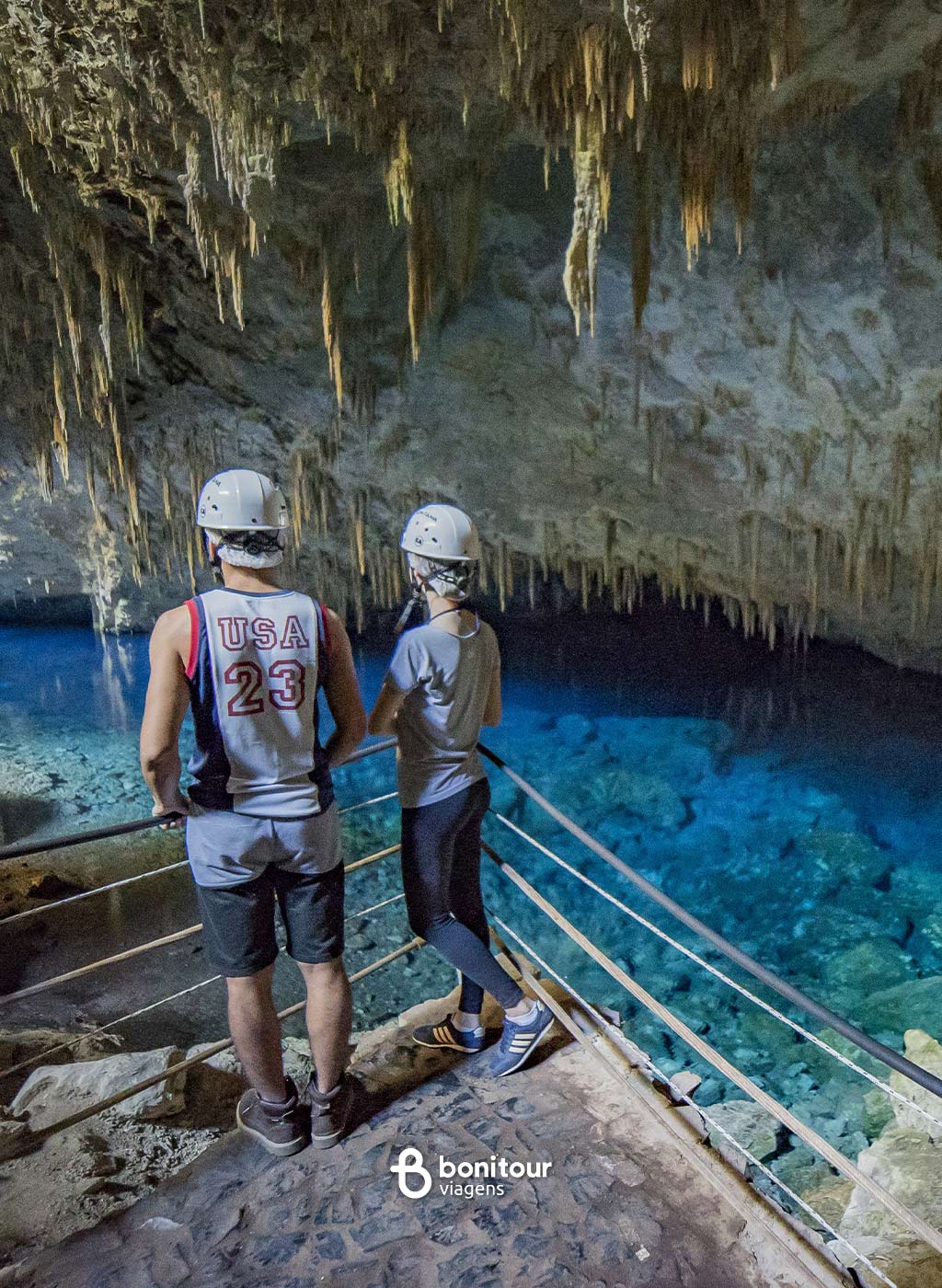 Pessoas contemplando vista da Gruta do lago azul com águas cristalinas azuis e formações rochosas