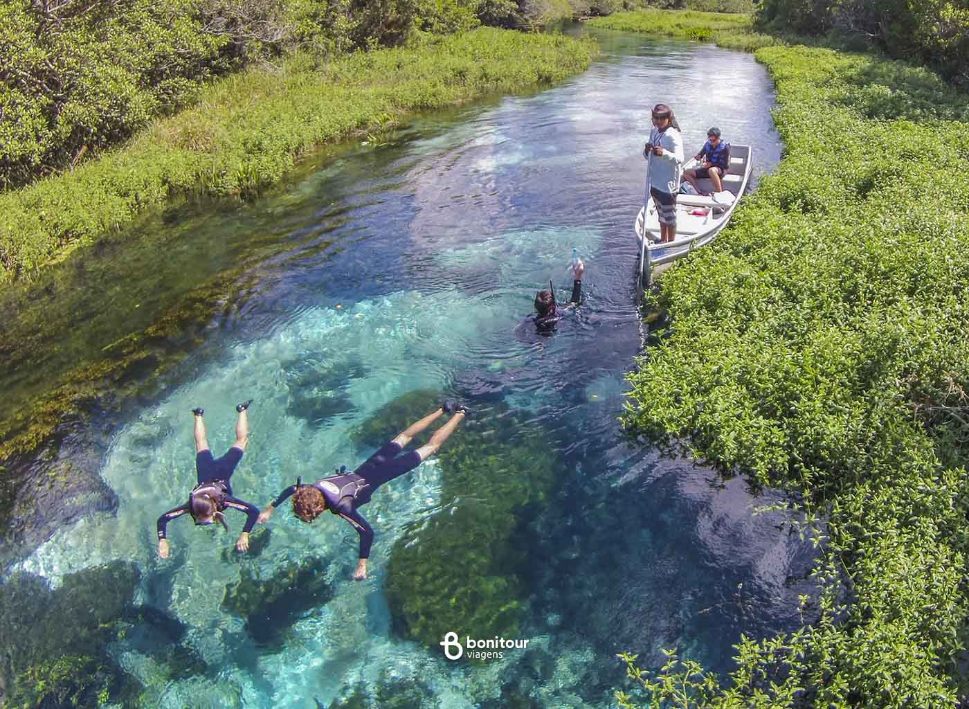 Pessoas em barco, observando outras pessoas fazendo flutuação no Rio Sucuri.