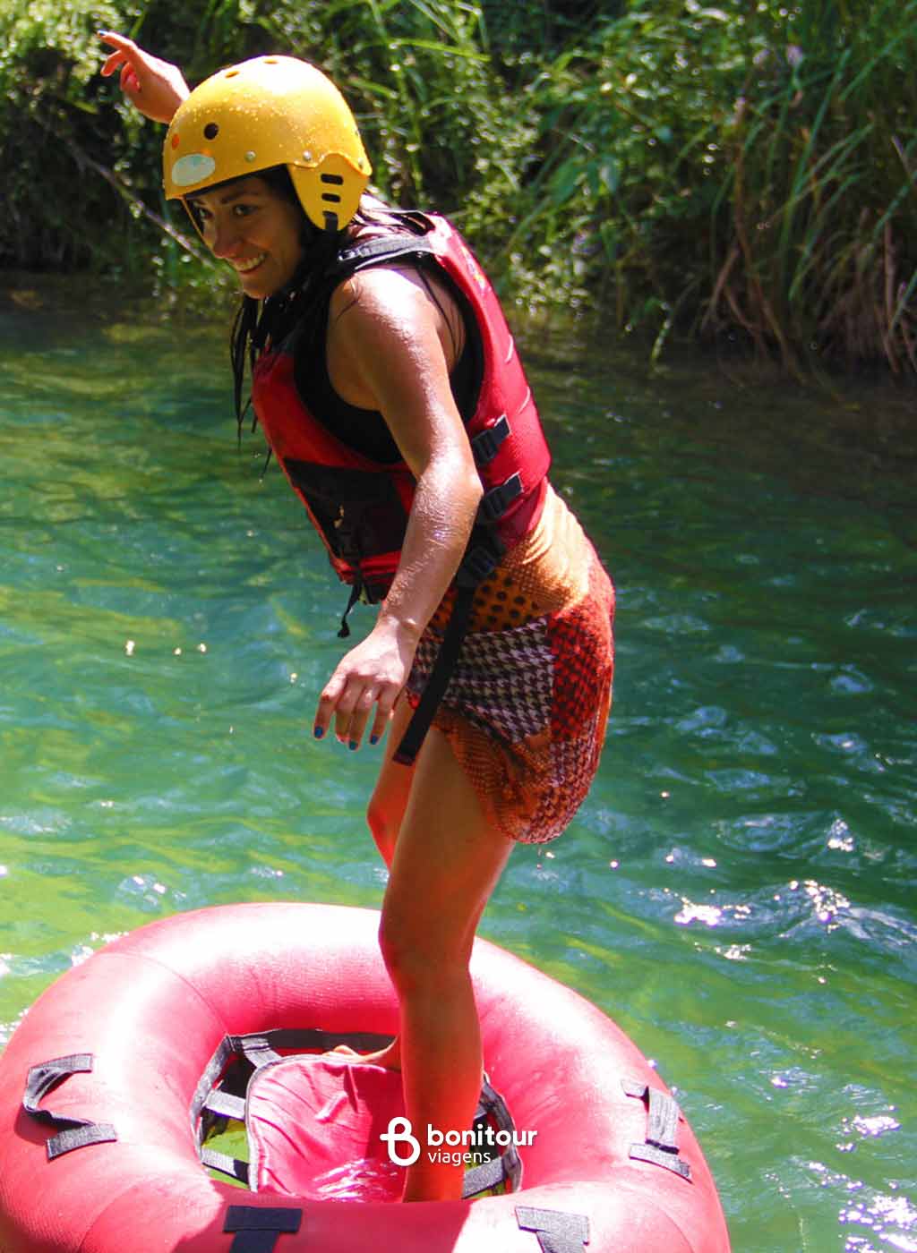Pessoa se equilibrando em pé em cima de boia na água com natureza ao fundo
