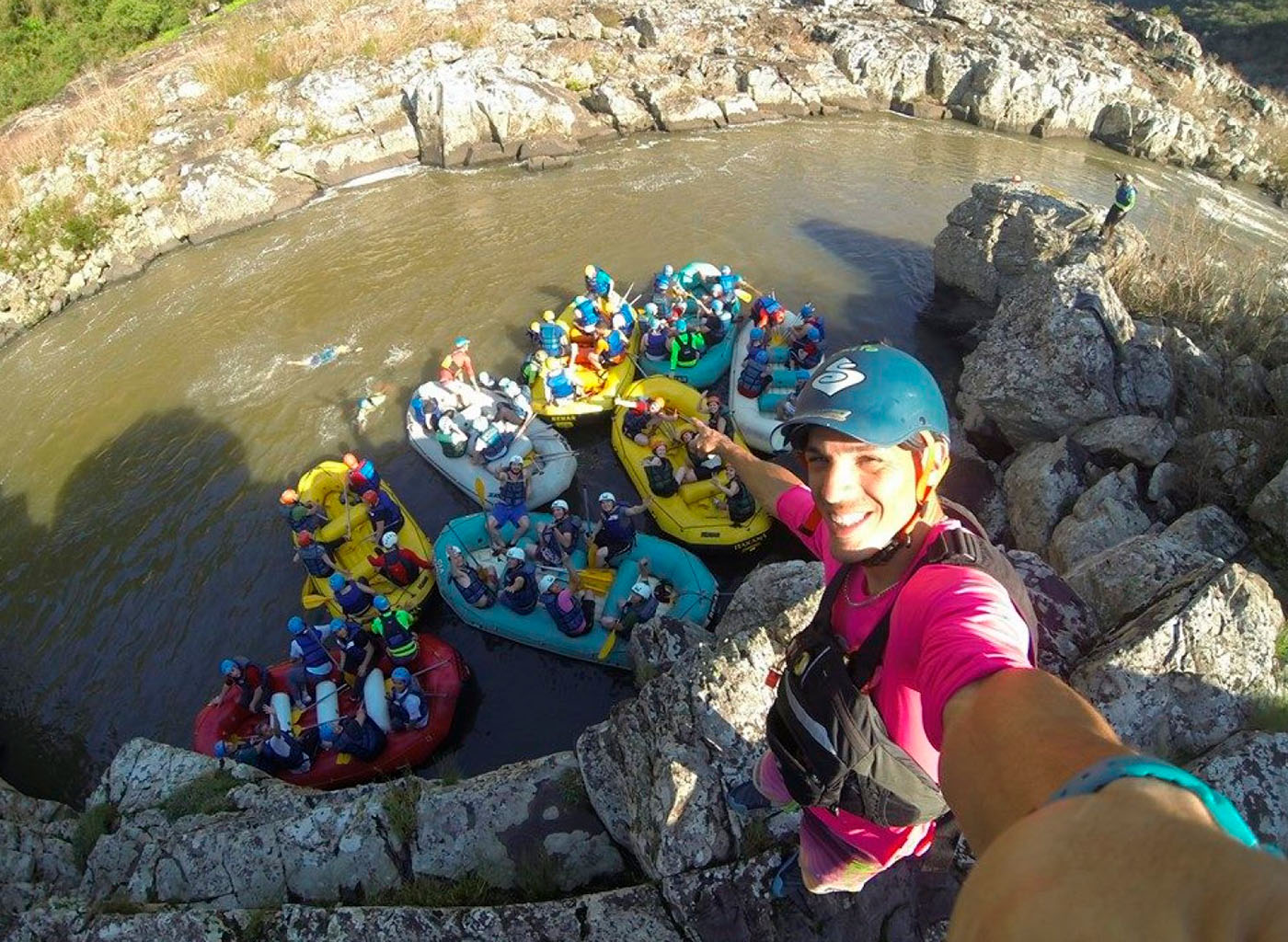 Pessoa no alto de pedra mostrando pessoas em botes infláveis abaixo dele, no Rio das Antas