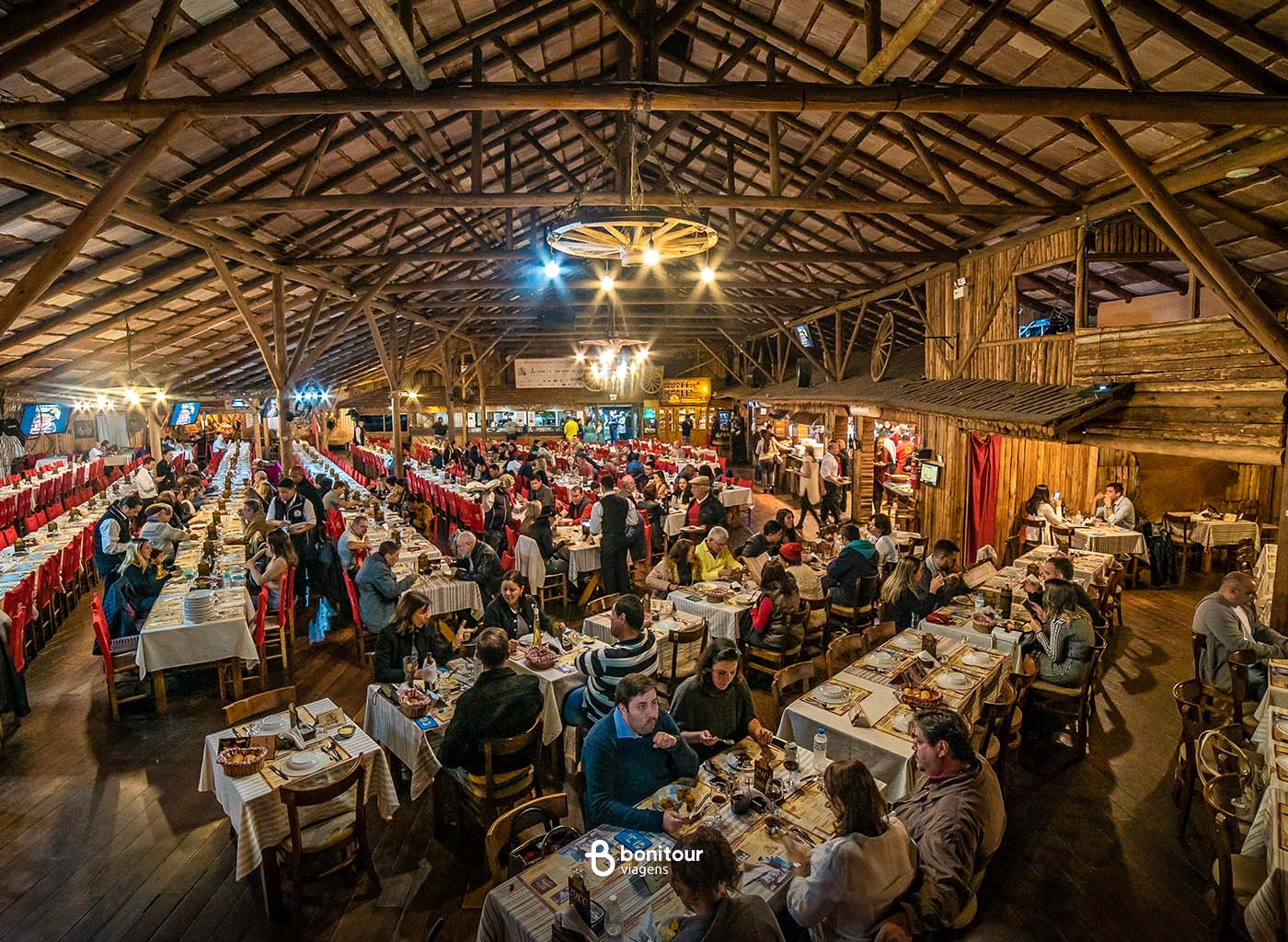 Vista de cima de dentro de galpão com várias pessoas à suas mesas jantando