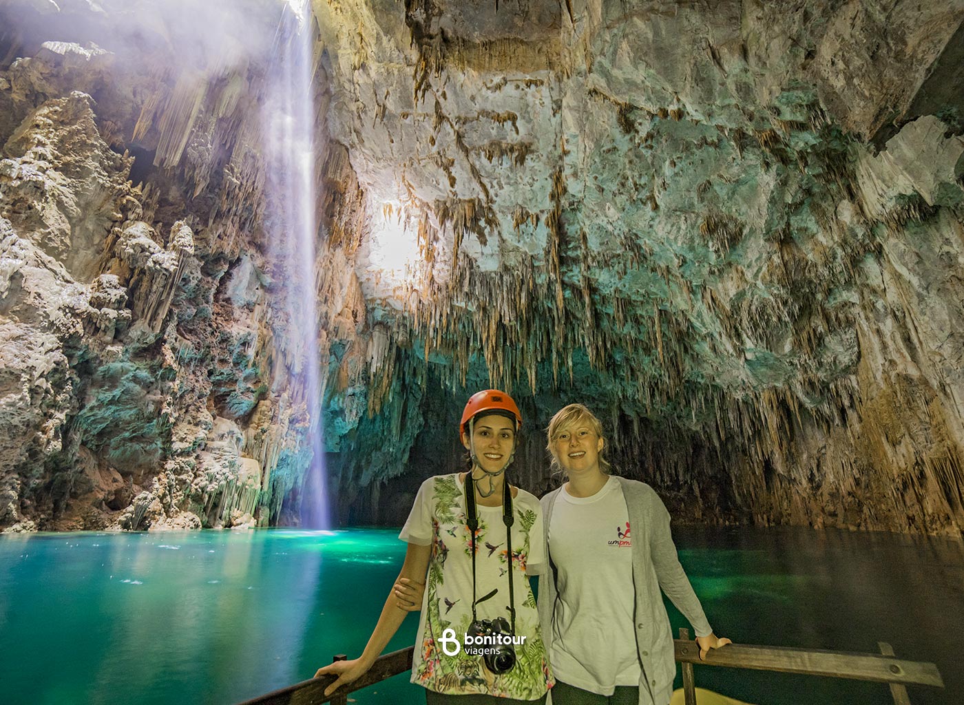 Duas pessoas em deck de madeira no Abismo Anhumas com águas cristalinas e formações rochosas