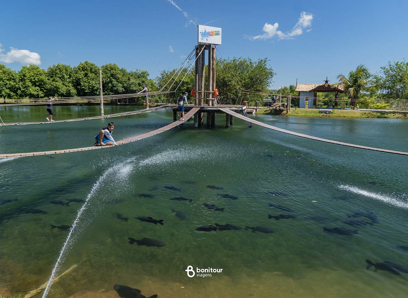 Pessoas andando em atrativo do Balneário Nascente azul, com vários peixes nadando nas águas