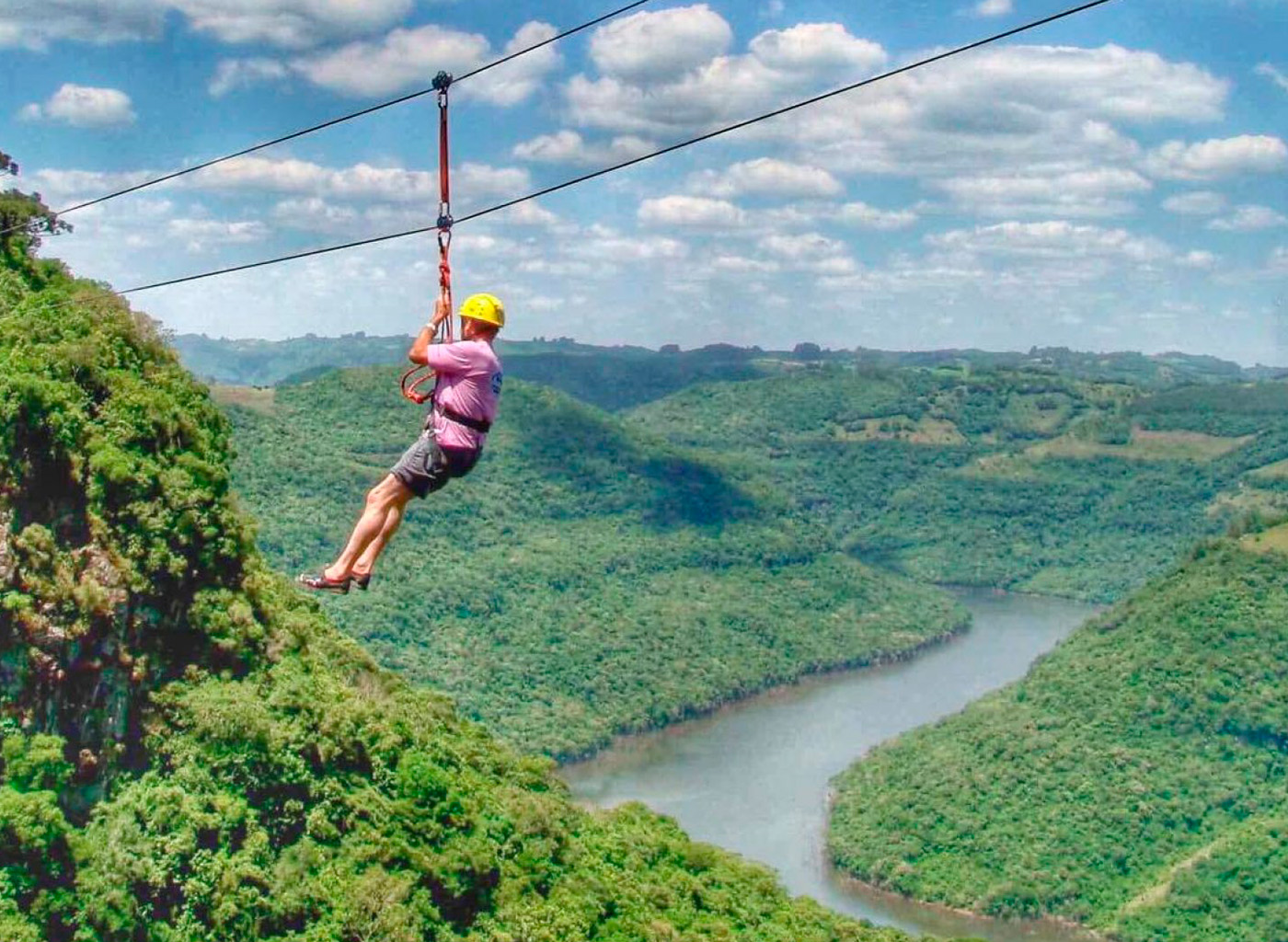 Pessoa descendo de tirolesa com paisagem de um rio ao fundo