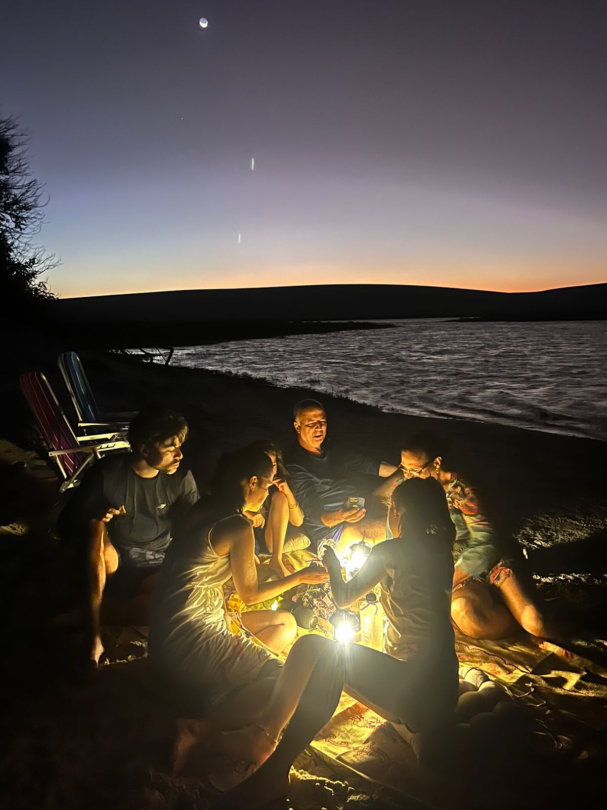 Turistas reunidos à beira da lagoa sob a luz das lanternas durante o Mirar das Estrelas
