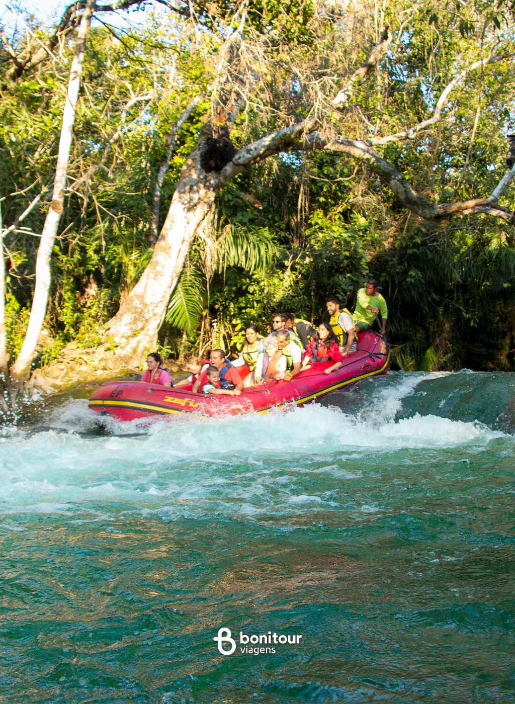 Pessoas descendo com bote inflável por pequena queda d'água em meio a natureza