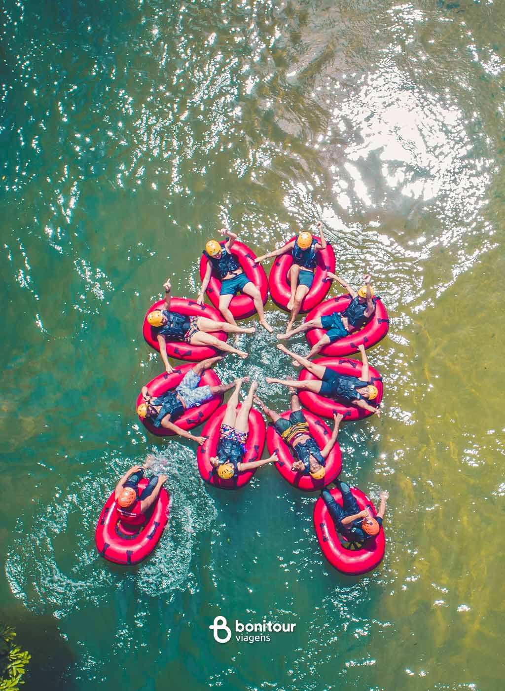 Vista de cima de várias pessoas deitadas em boias de mãos dadas na água