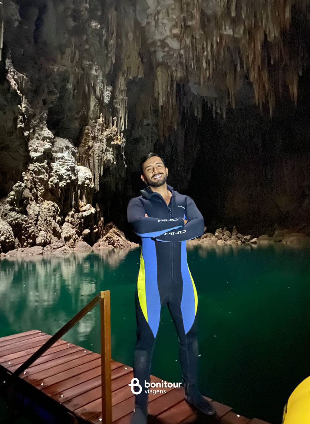 Pessoa com roupa de neoprene dentro do Abismo Anhumas com águas cristalinas e formações rochosas