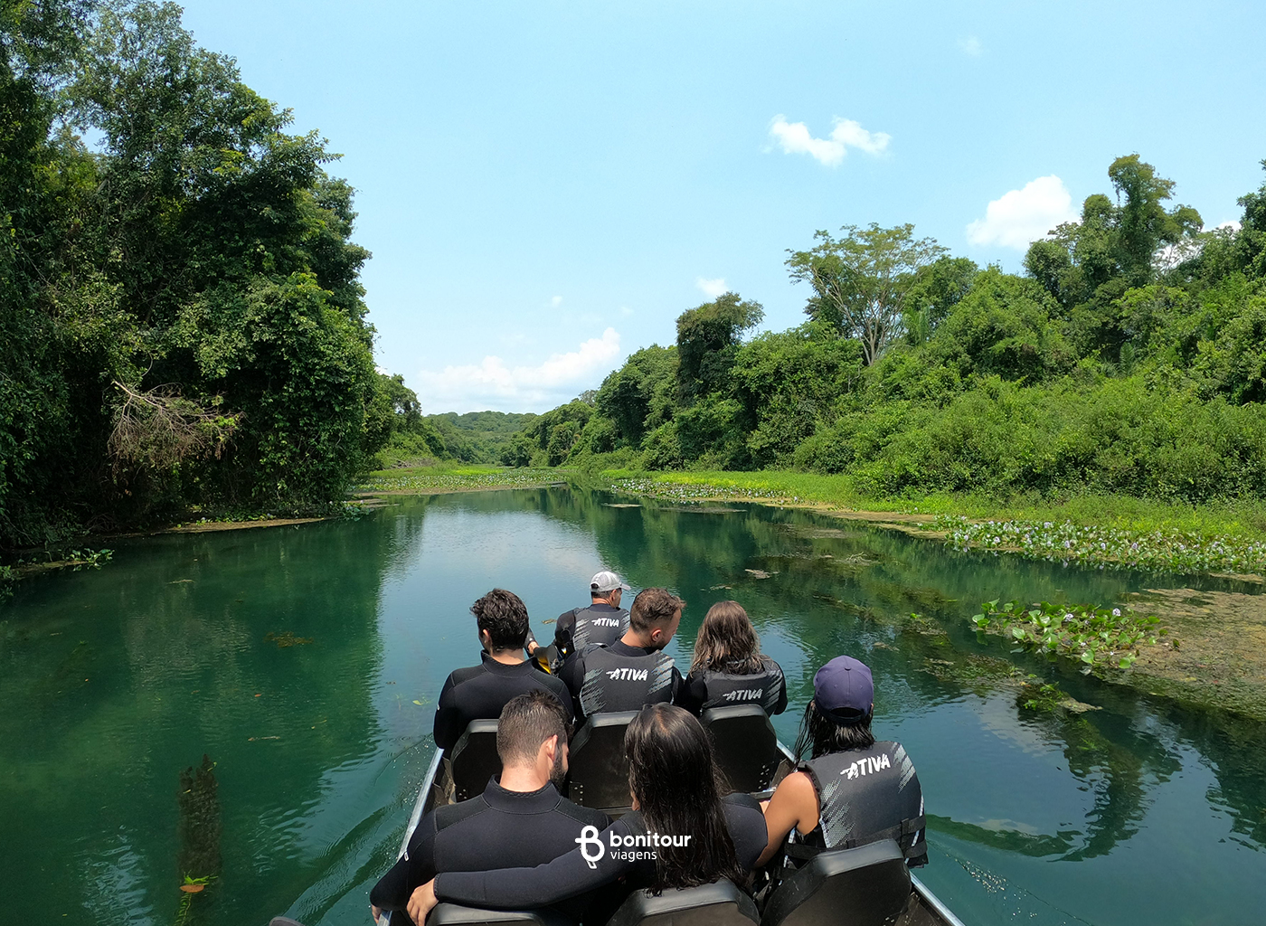 Pessoas em barco, navegando pelo Rio Azul, em meio a vegetação