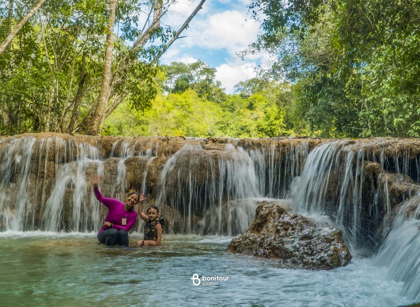 Pessoas acenando em frente à cachoeira da Estância Mimosa em Bonito/MS.