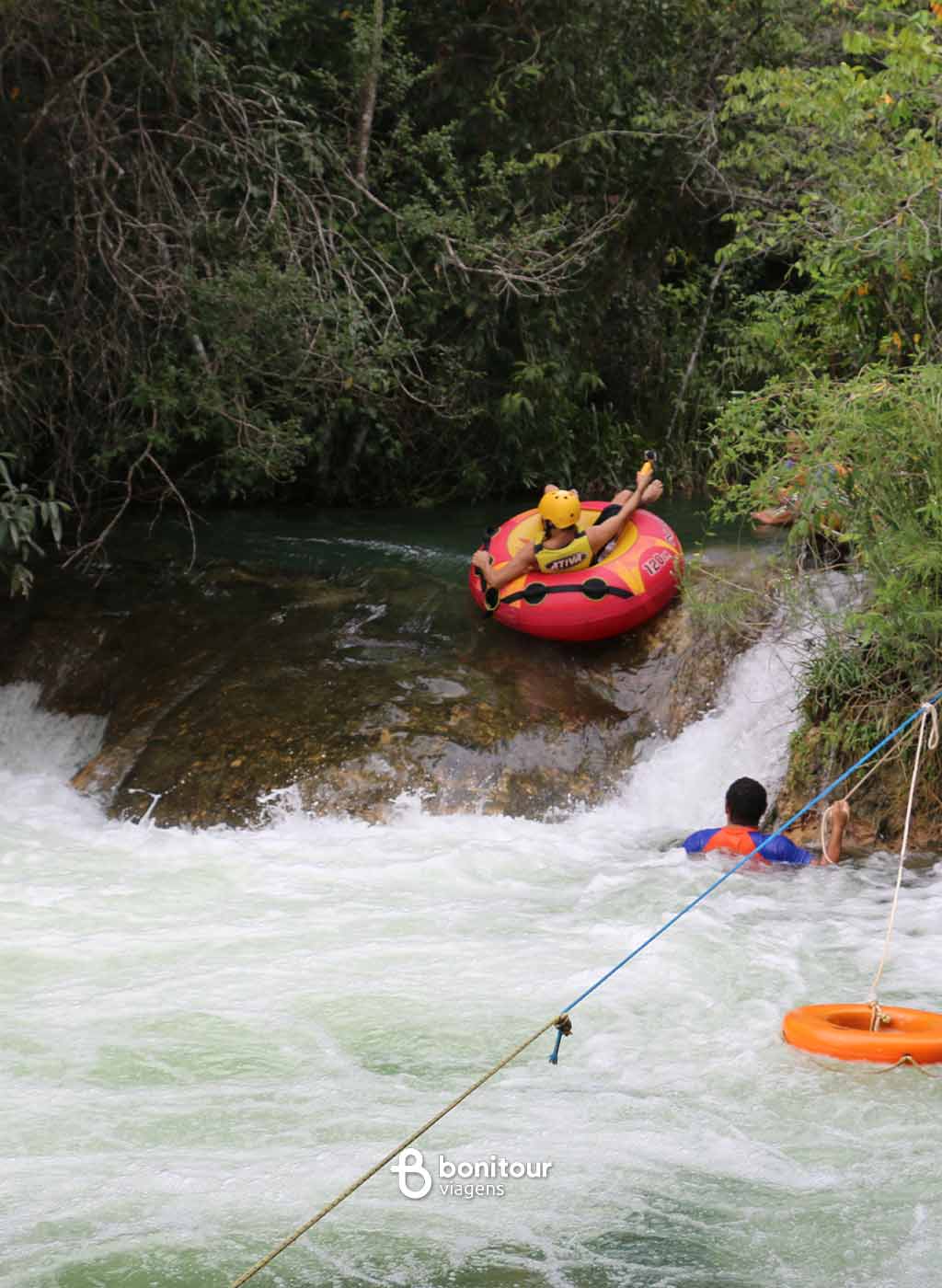 Pessoas descendo de boia cross em queda da água com equipamento de proteção.