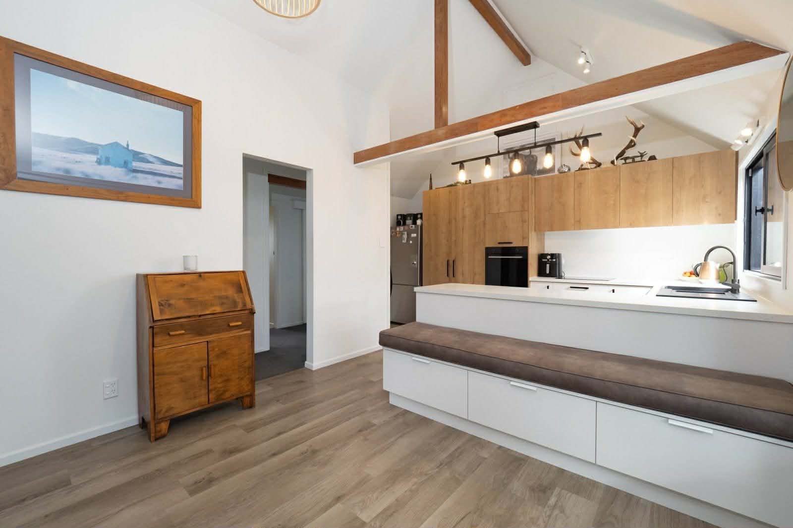 Interior view of a modern kitchen with white countertops, wooden cabinetry, exposed wood beams, and a large island with seating.