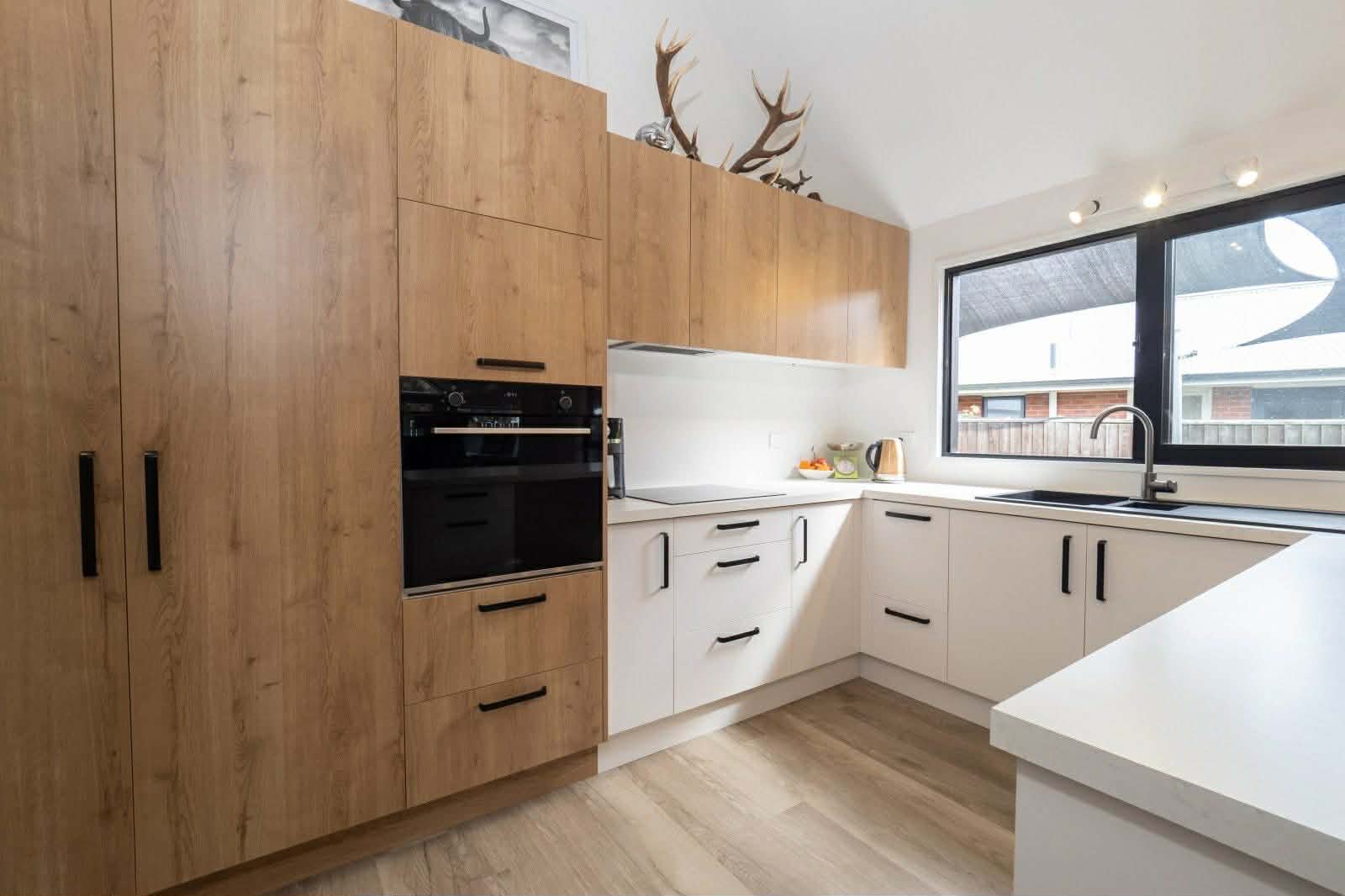 Modern kitchen interior with two-tone cabinetry featuring natural wood and white units, built-in black appliances, and wood-effect flooring.