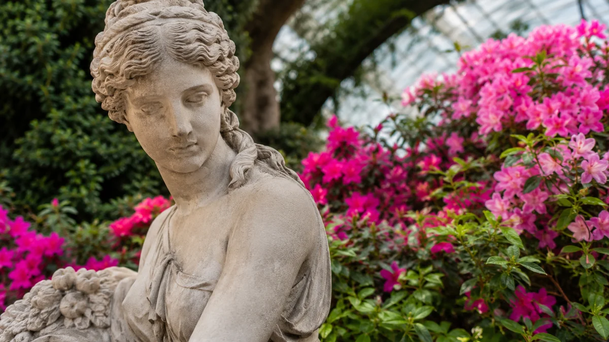 A classical ornamental statue surrounded by seasonal blooms in a conservatory garden.