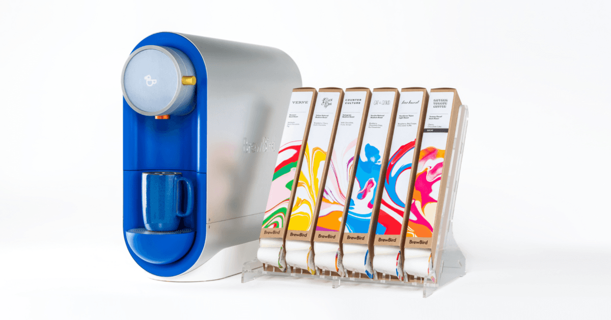The BrewBird machine beside a rack of colorful compostable whole-bean coffee pods