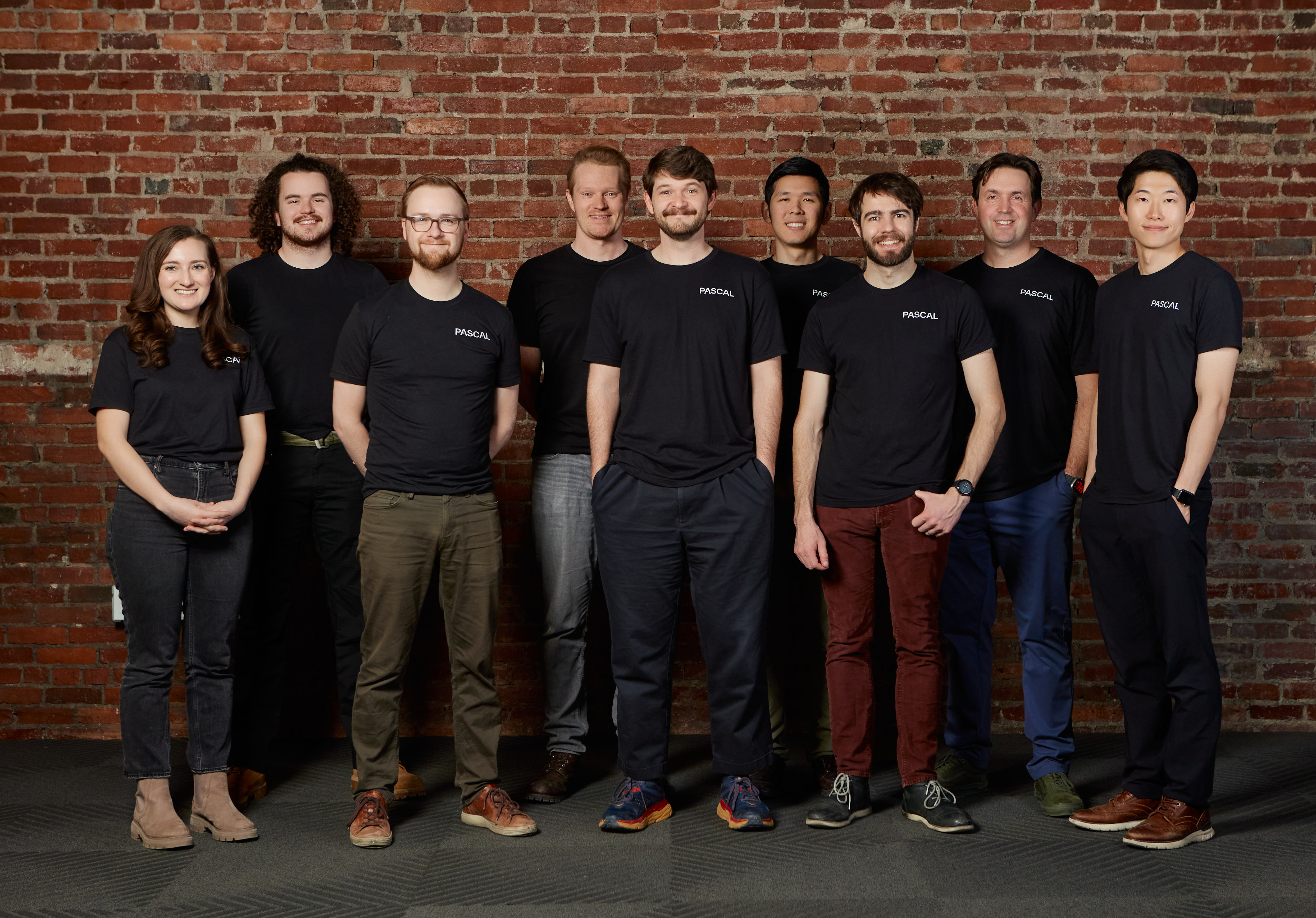 The Pascal team in matching branded t-shirts against a brick wall