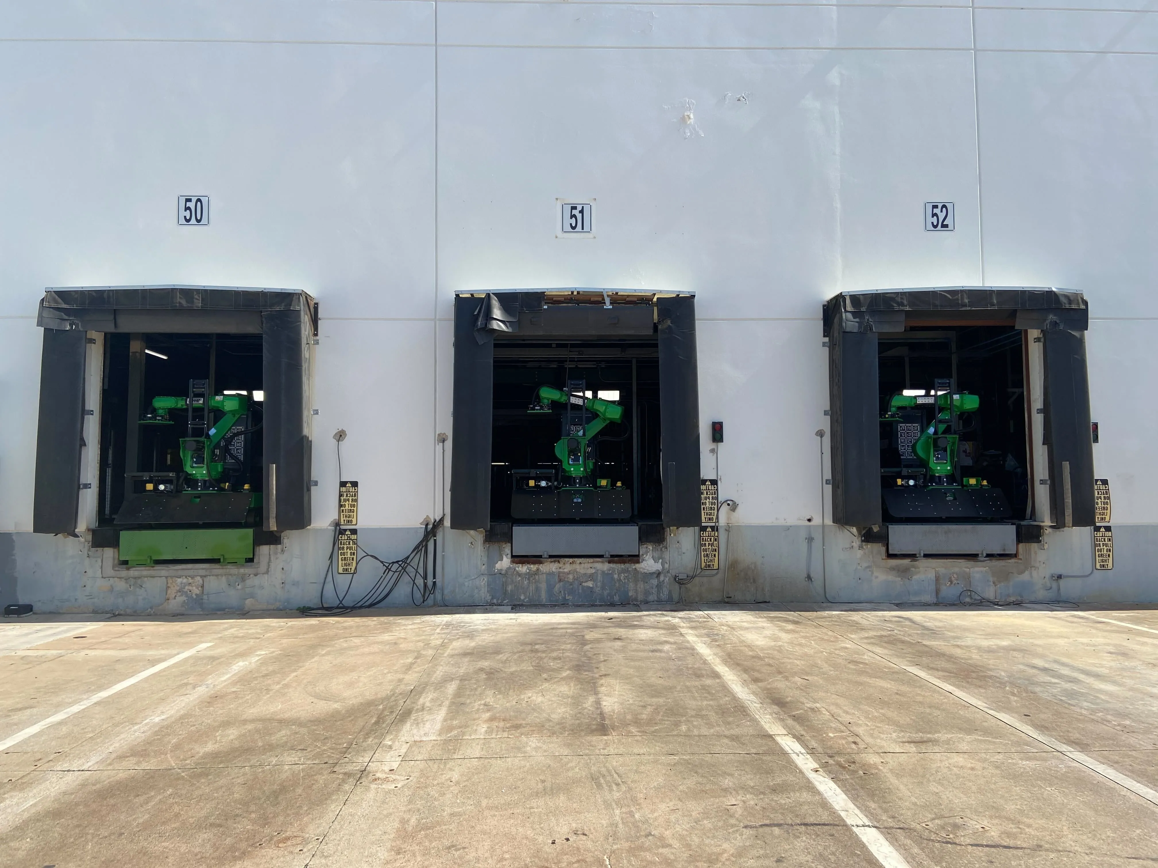 Three Pickle Robot unloading systems lined up at warehouse loading docks, ready to unload trailers