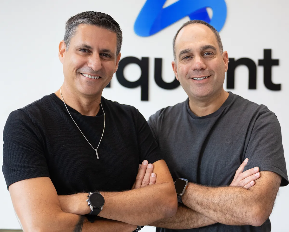 Shahar Chen, arms folded, in front of the Aquant logo, standing next to co-founder Assaf Melochna
