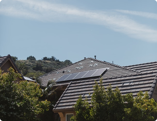 Suburban tile roof with a small solar array against a blue sky and hills