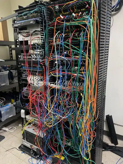 Old network rack with disorganized cabling before Ubiquiti upgrade at manufacturing facility