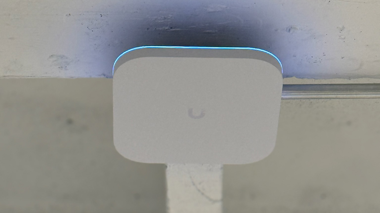 Ceiling mounted UniFi access point with glowing blue LED indicator and professional cable management conduit