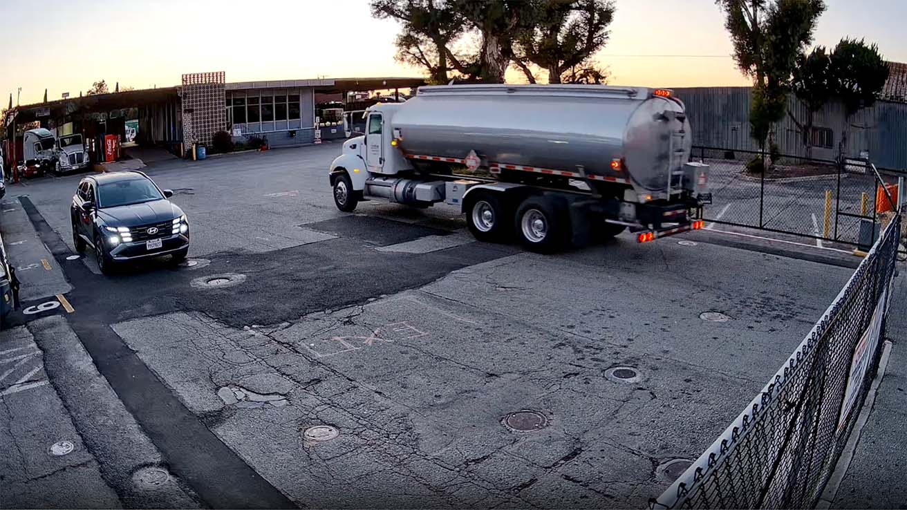 Tanker truck with Hazmat placards entering commercial yard monitored by security cameras