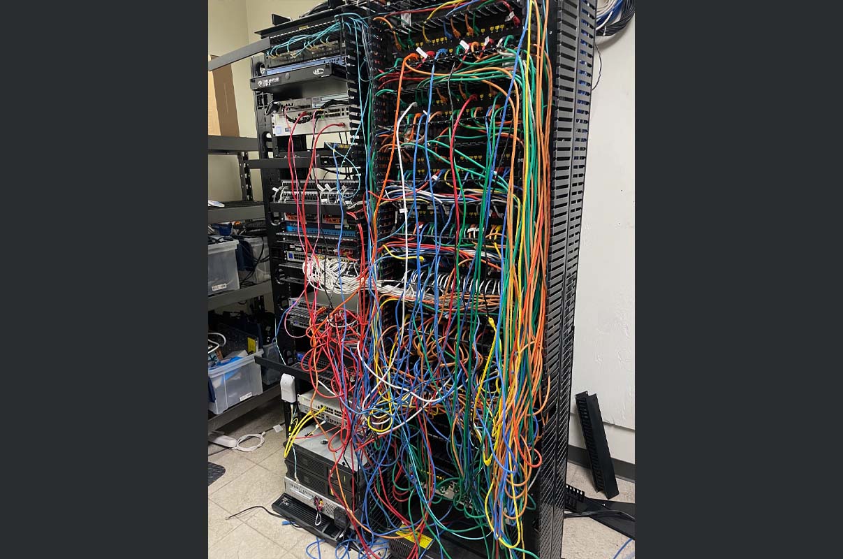 Old network rack with disorganized cabling before Ubiquiti upgrade at manufacturing facility