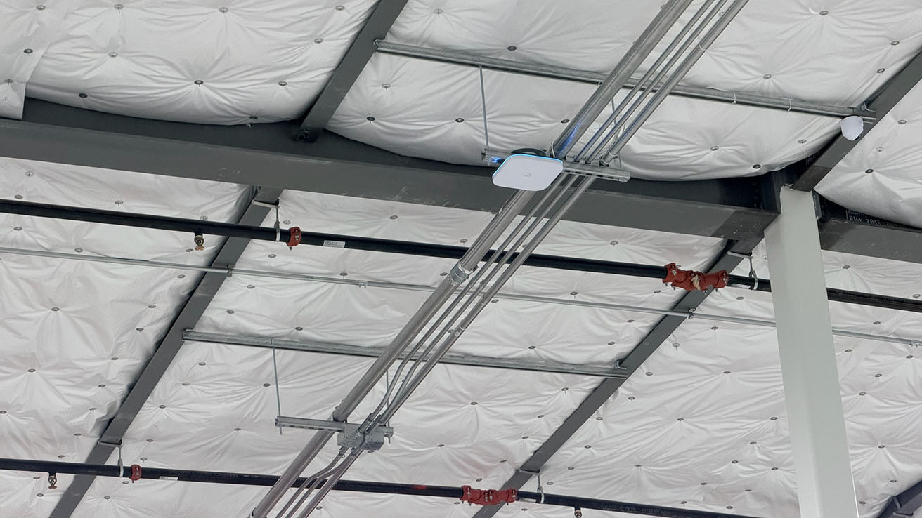 Commercial wireless access point installation on a warehouse ceiling with professional structured cabling