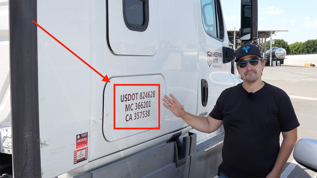 Engineer pointing to USDOT registration numbers and door panel identifiers on a commercial truck