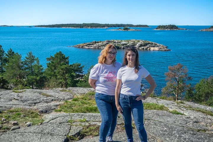 Two women, rocky coast, blue sea, islands.