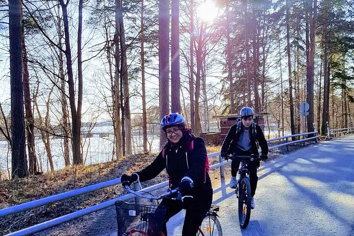 Two cyclists biking sunny forest by lake.