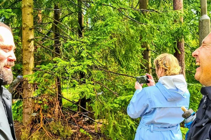 Woman photographs forest while two men laugh.