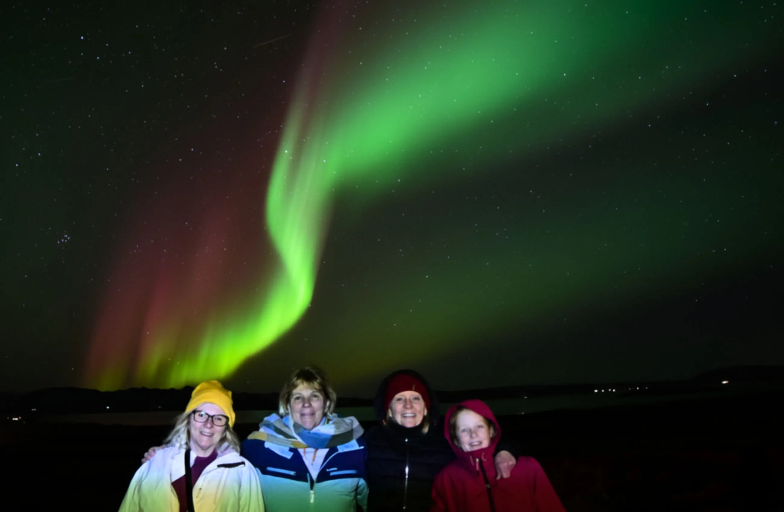Four people smiling under Northern Lights.