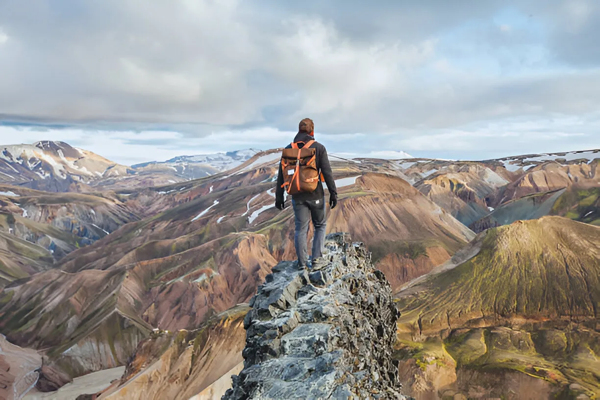 Hiker on mountain peak overlooking colorful landscape.