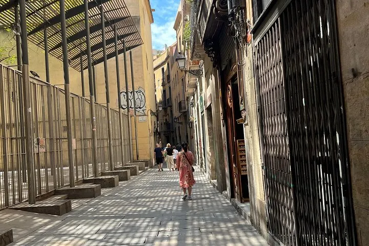 Sunlit urban street with people and patterned shadows.