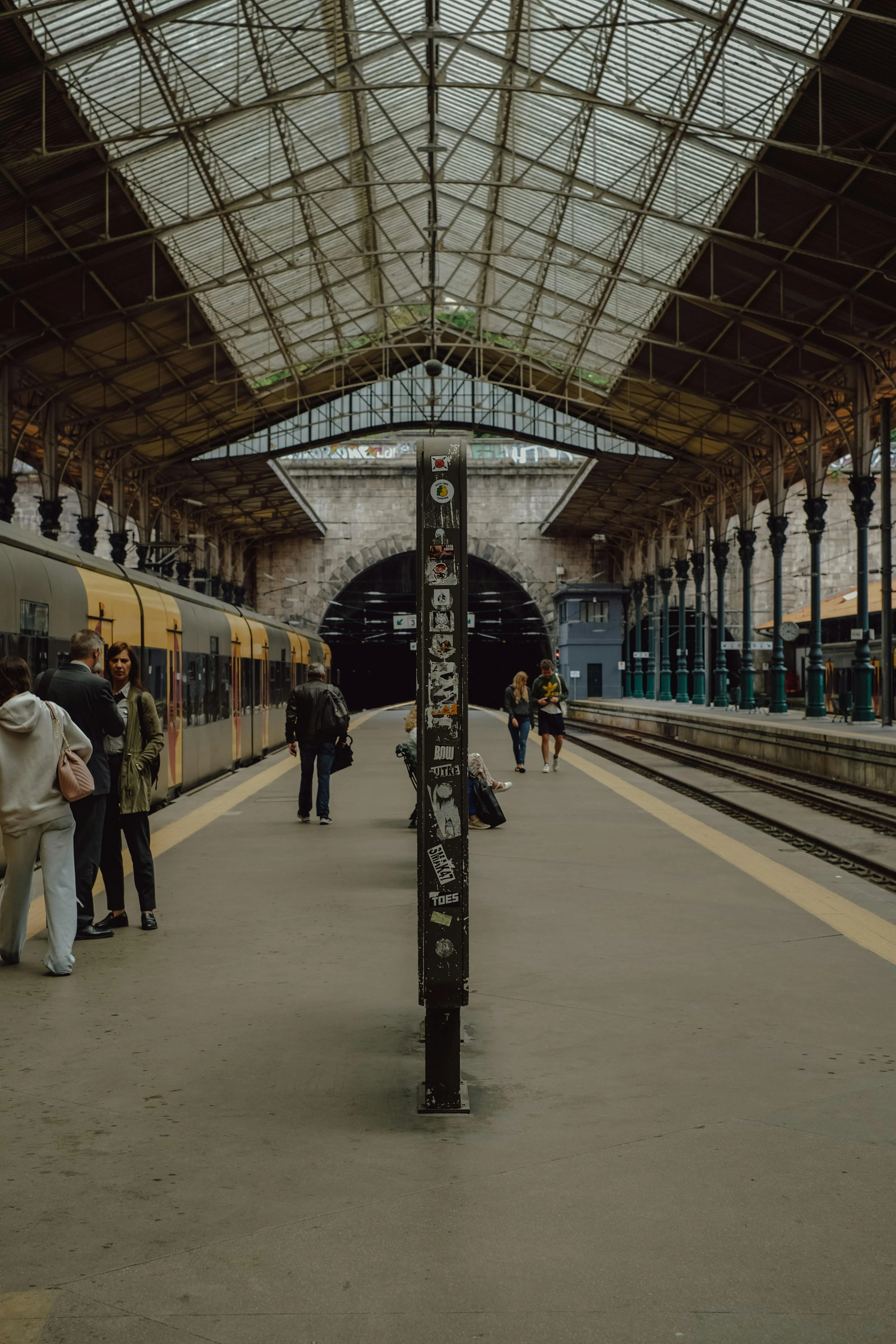 Historic train station platform, passengers, train, vaulted roof.