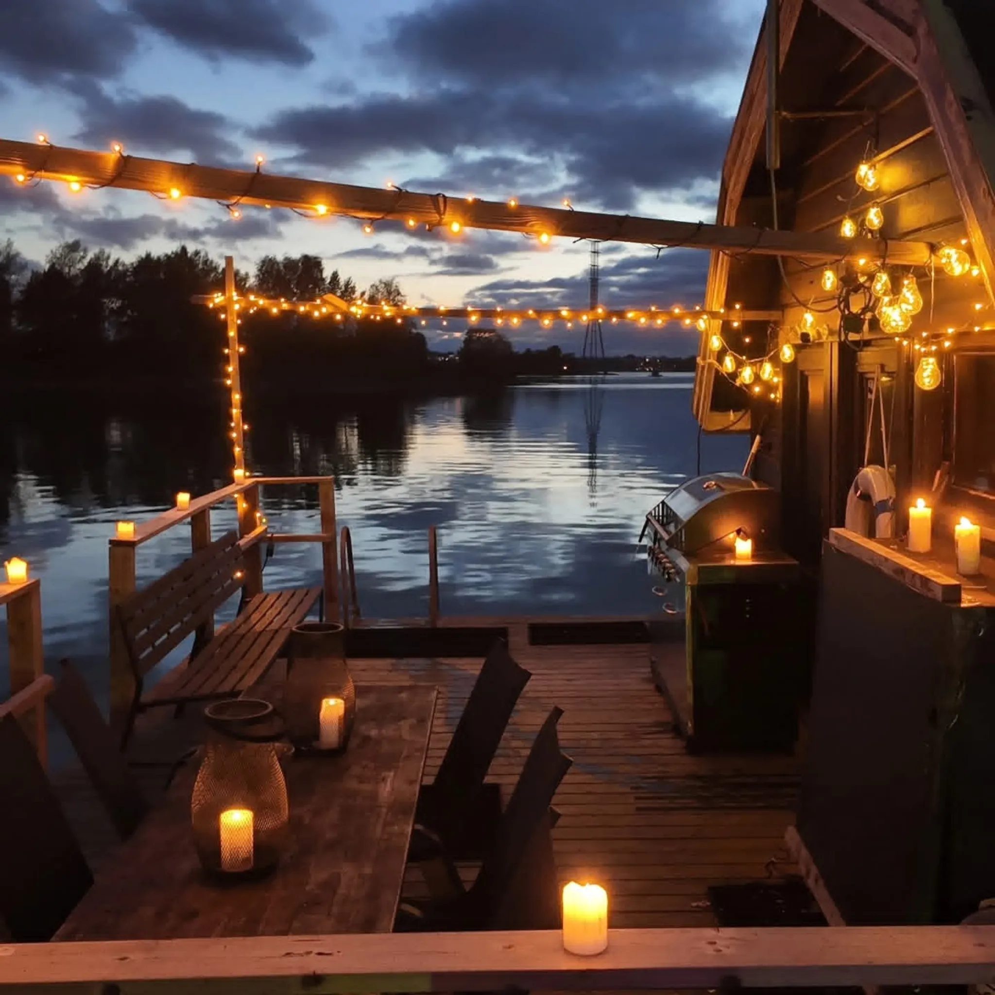 Waterfront deck with string lights and candles at night.