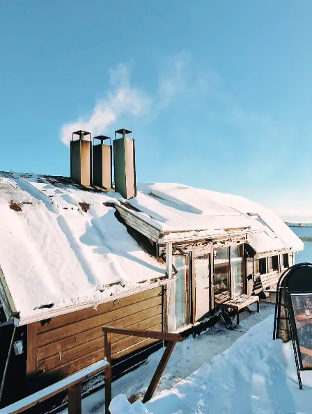 Snowy wooden cabin with smoking chimneys.