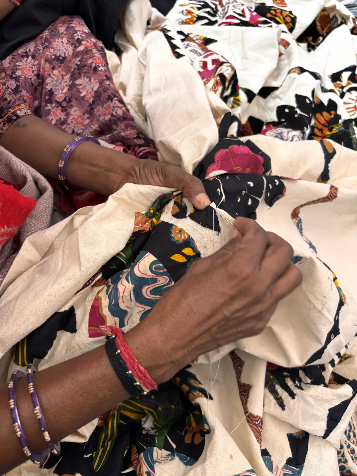 An artisan's hands drawing a needle through appliqué cloth, stitching the motif down