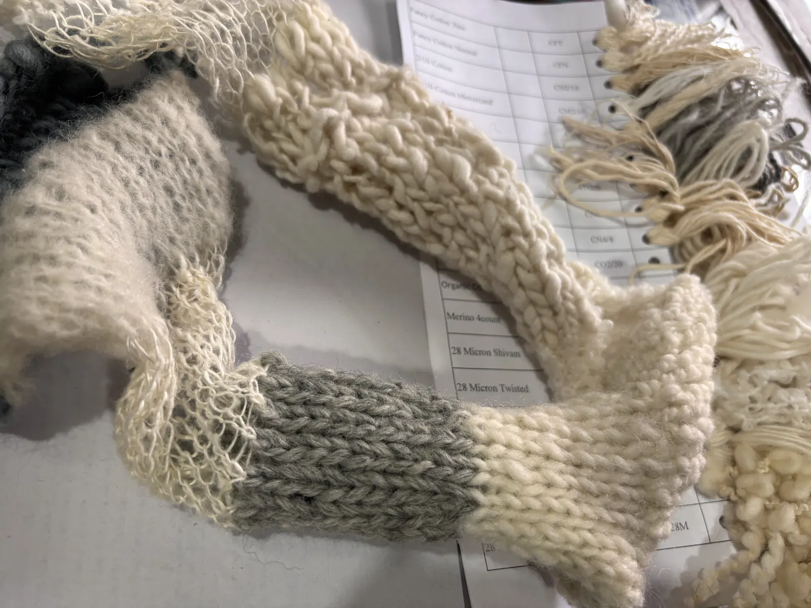 Hand-knitted yarn samples resting on a specification card that records each yarn count