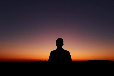 Silhouette of a person gazing at a hopeful dawn horizon.