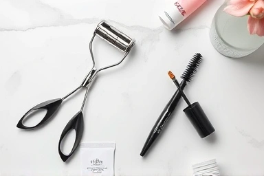 Heated eyelash curler and mascara on a marble surface.