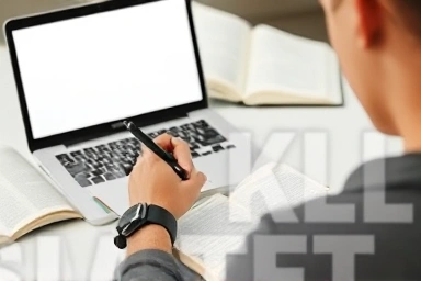 Person writing in journal, surrounded by books and laptop