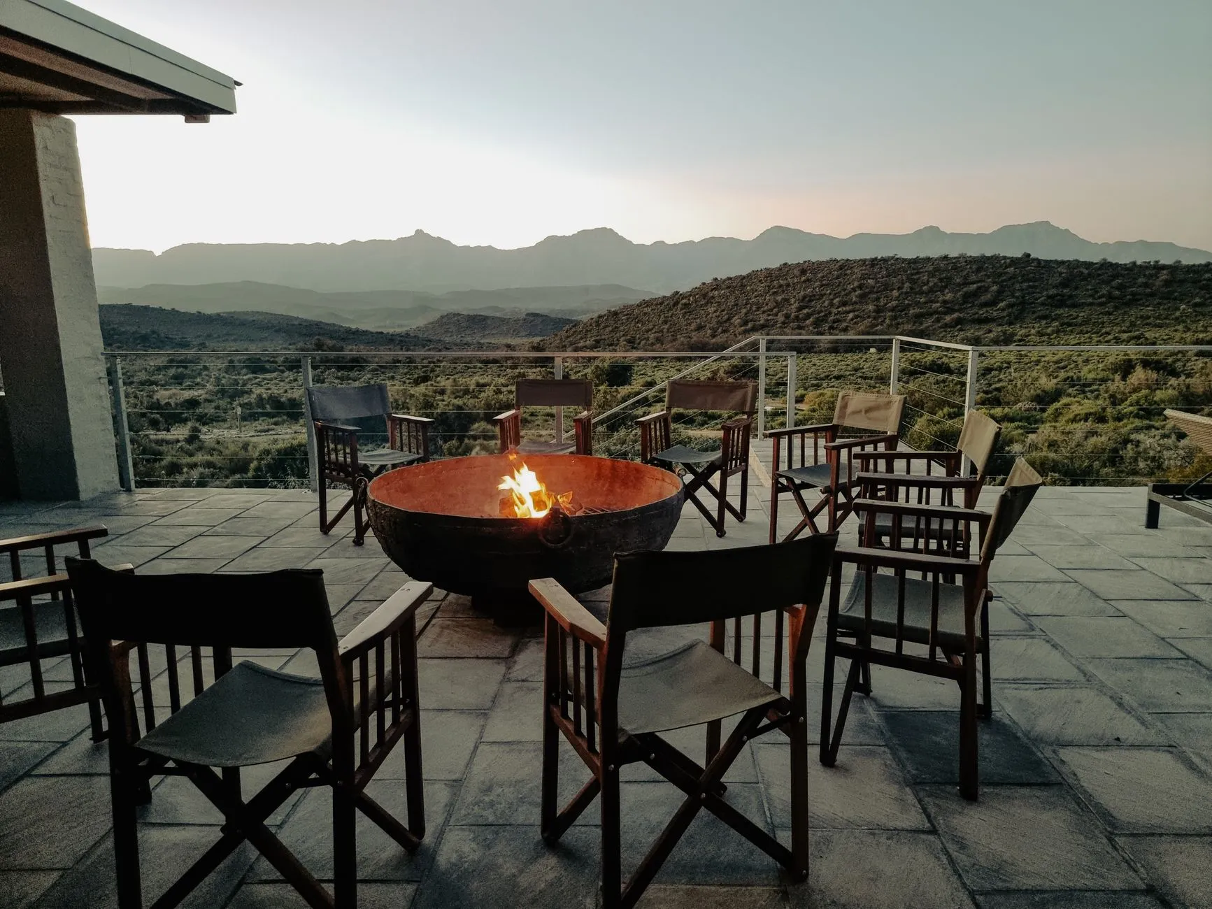 A fire bowl and chairs on a terrace looking out over high-desert hills at dusk