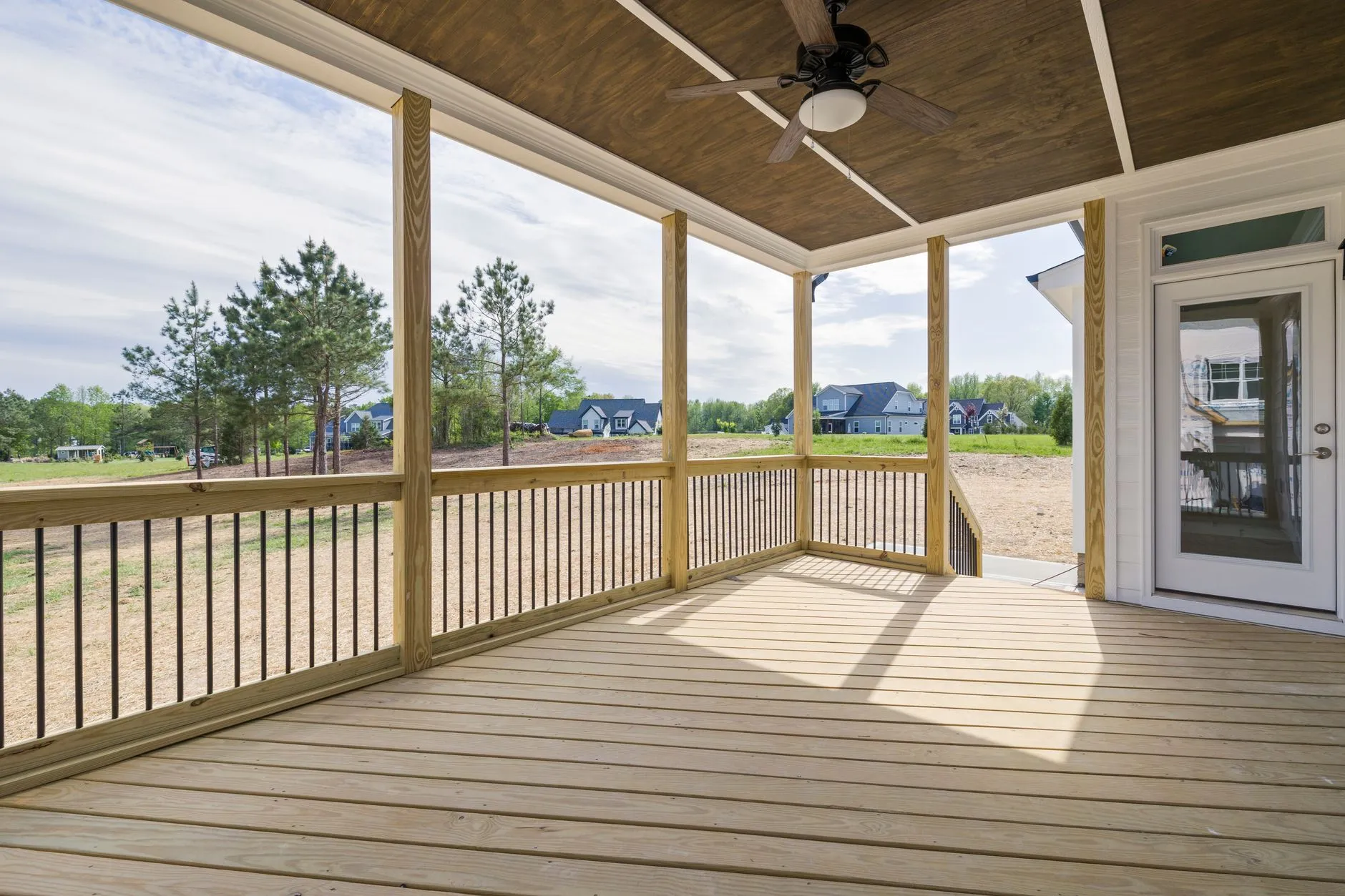 A covered timber deck with railings and a ceiling fan, looking out to trees