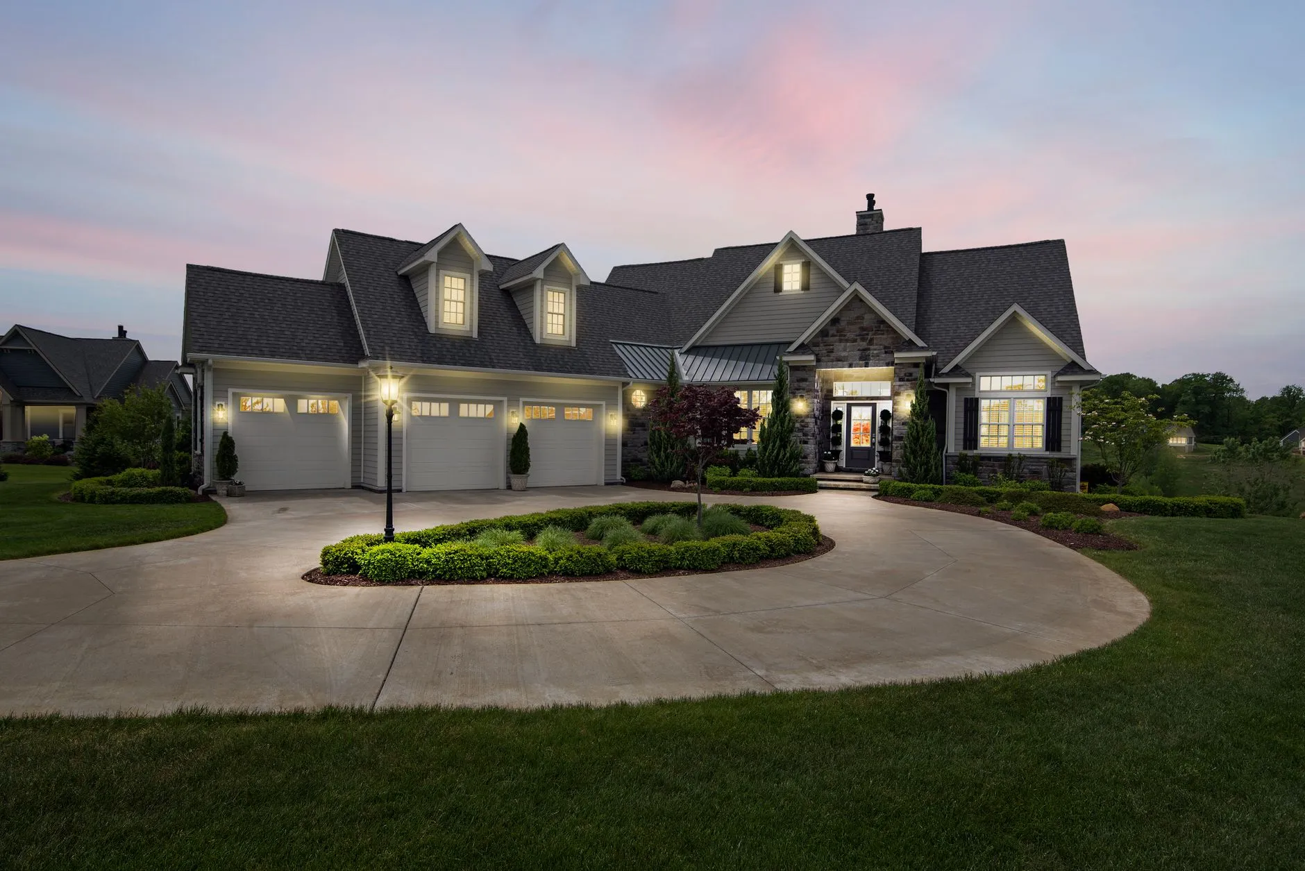 a large custom home at dusk with a curved drive and warm lit windows