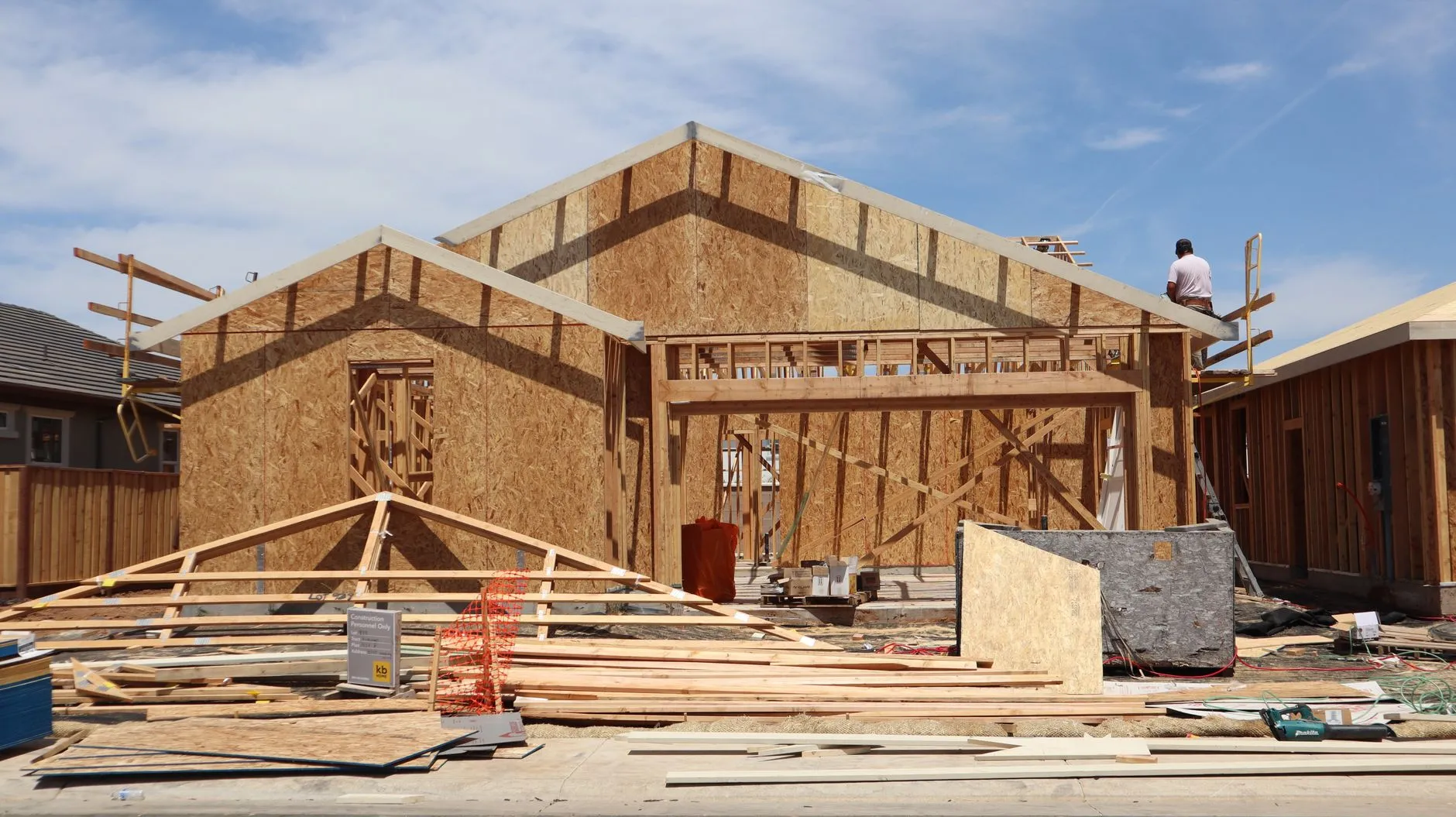 a framed and part-sheathed house with a worker up on the roof line