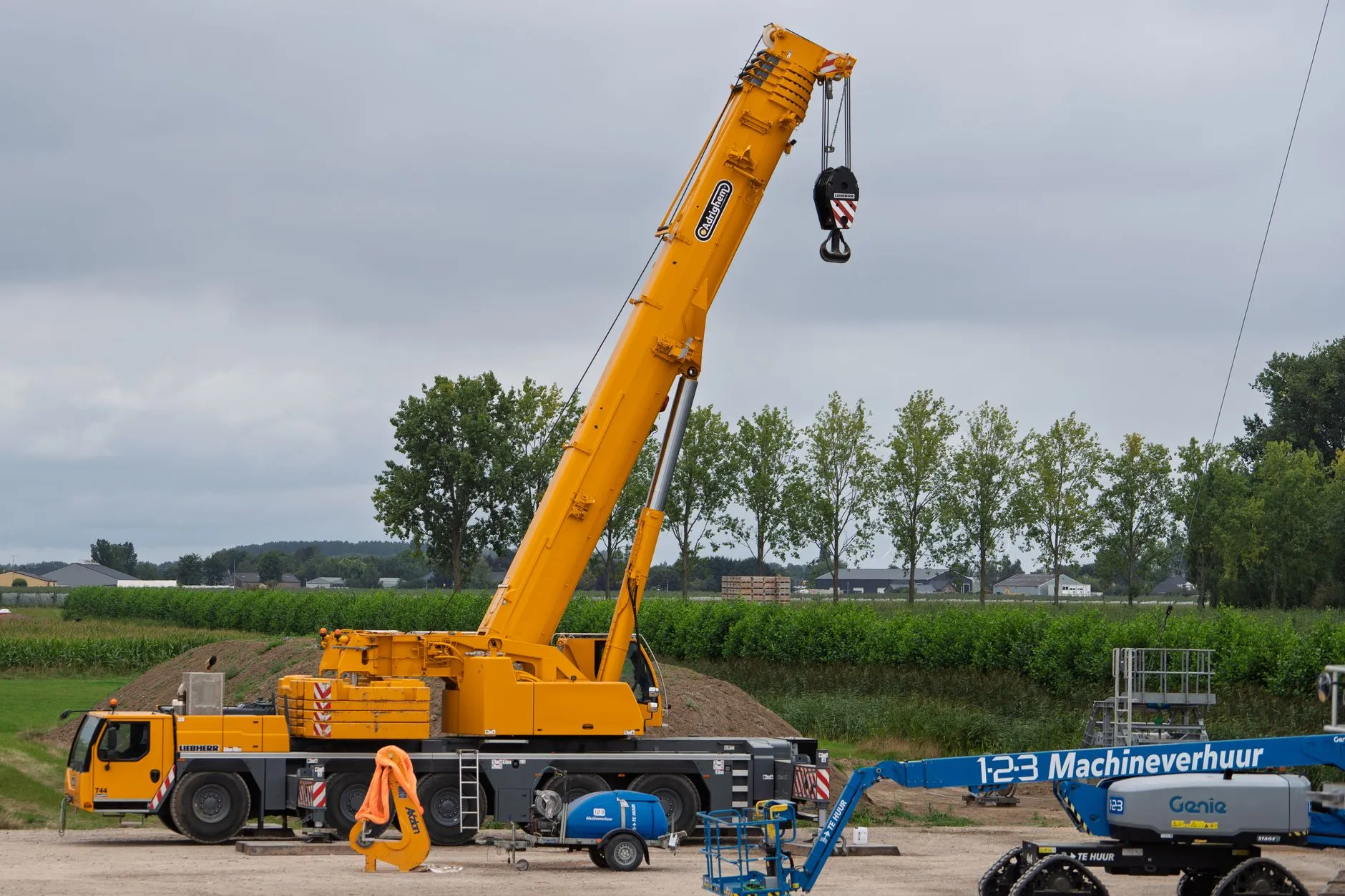 A yellow mobile crane set up with its boom raised on open ground