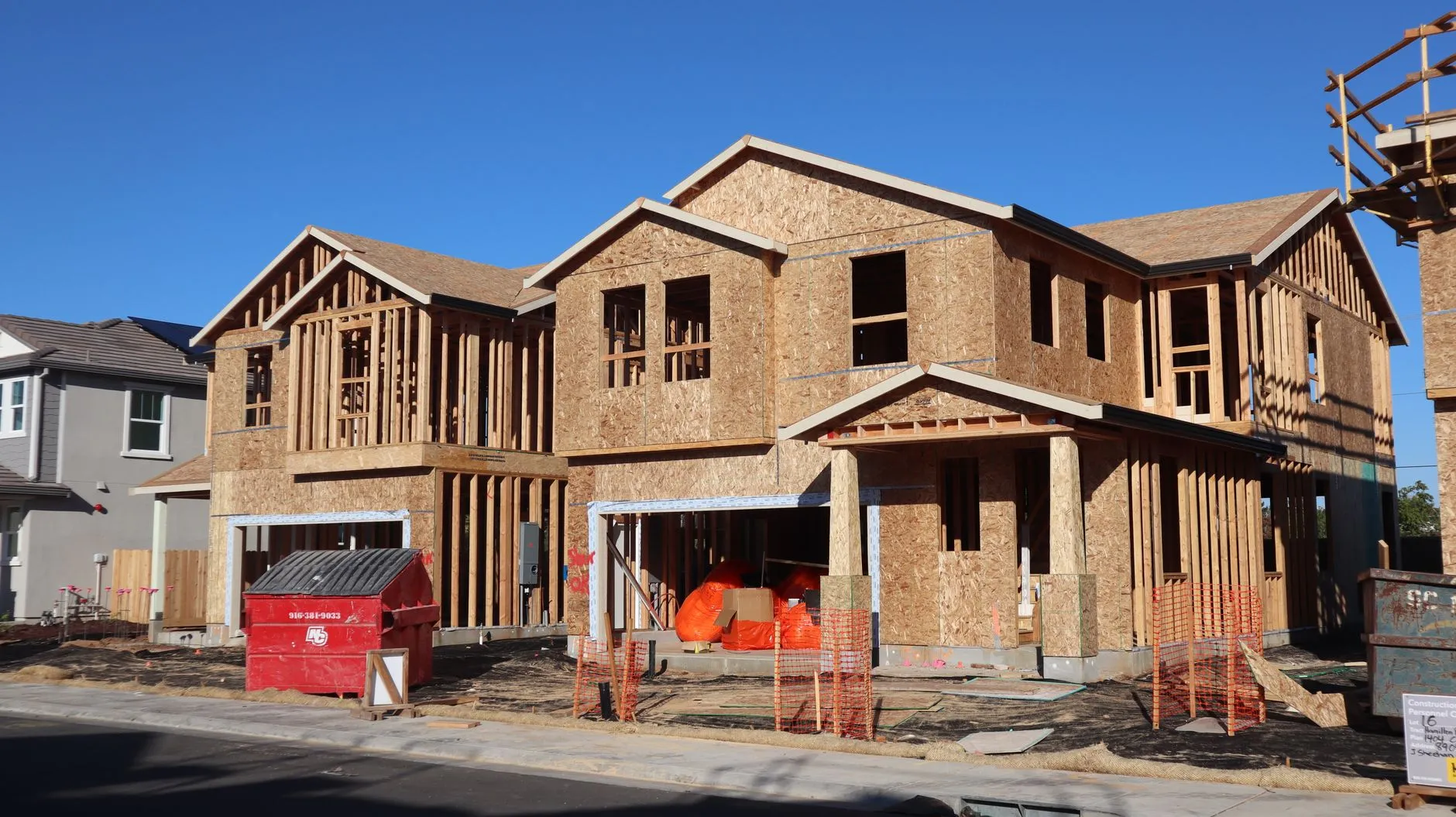 Two houses framed and sheathed on a residential street, built to code like any other